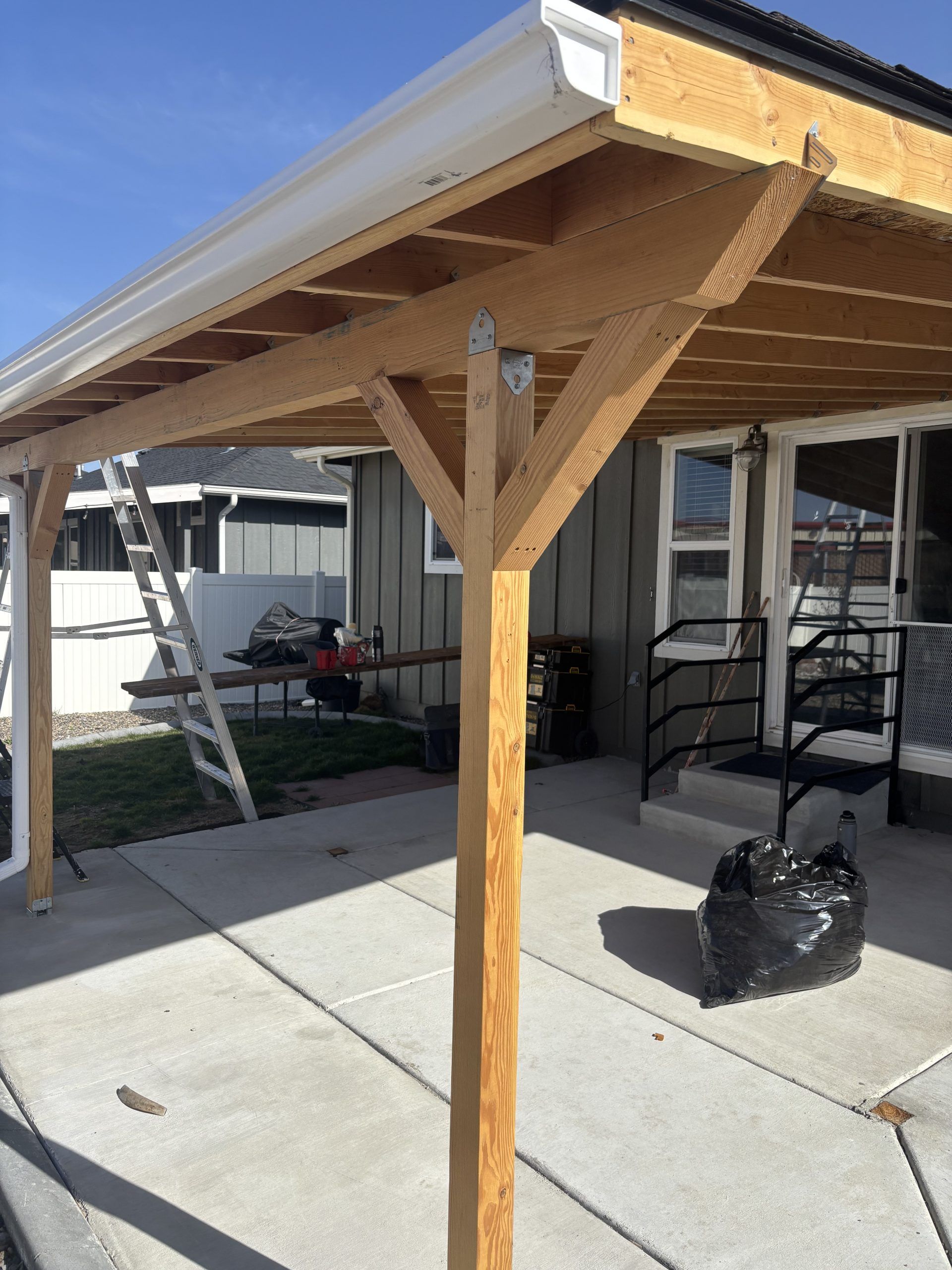 Wooden patio awning with support posts beside a house on a concrete slab