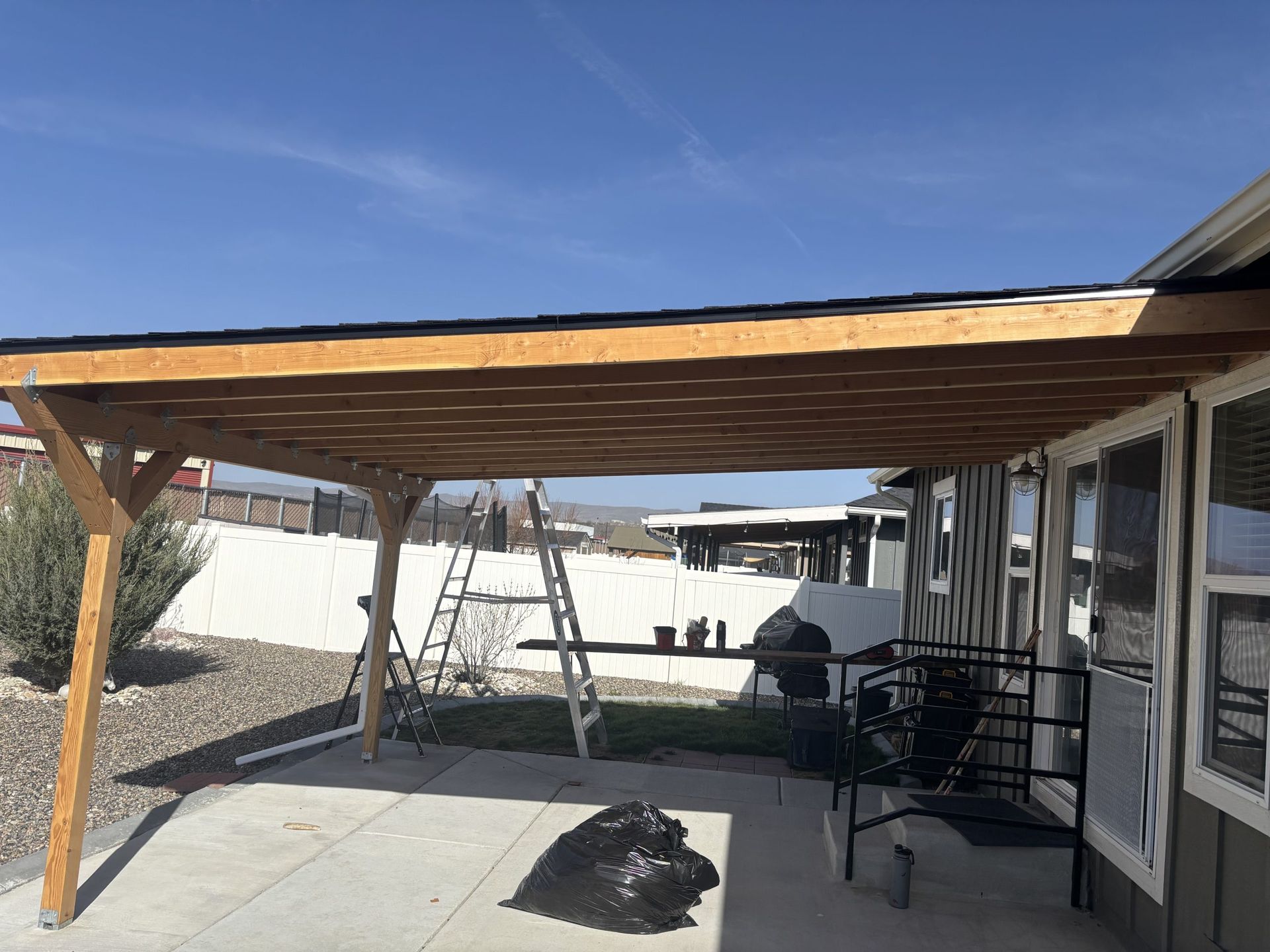 Covered patio with wooden pergola, concrete floor, bench, and desert landscaping under a blue sky