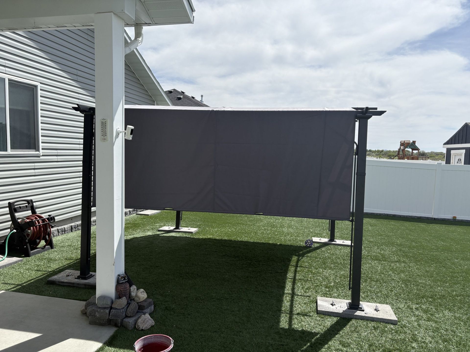 Gray outdoor privacy screen attached between white posts on a grassy patio beside a house