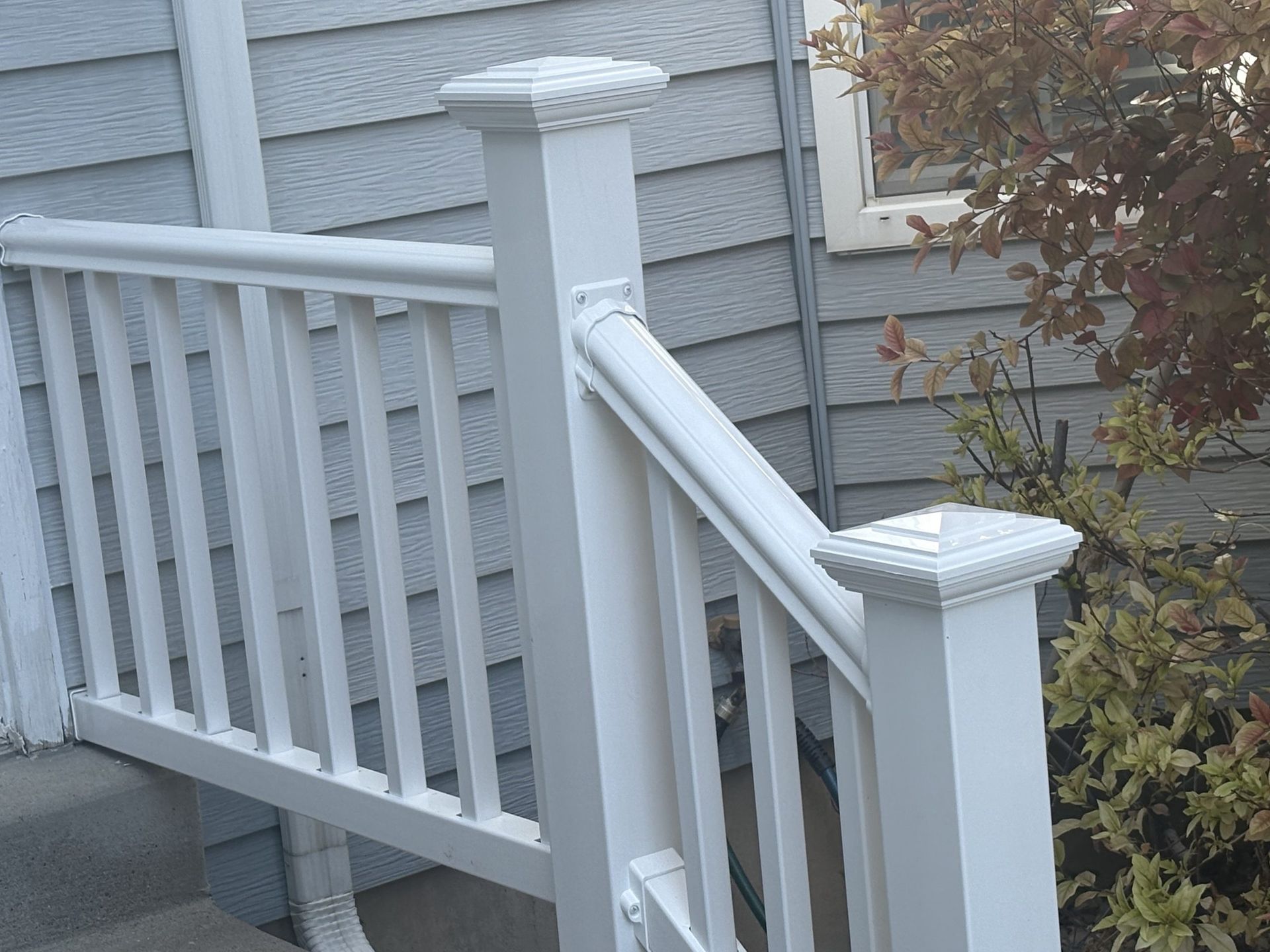 White wooden porch railing and steps beside a gray house and shrubs