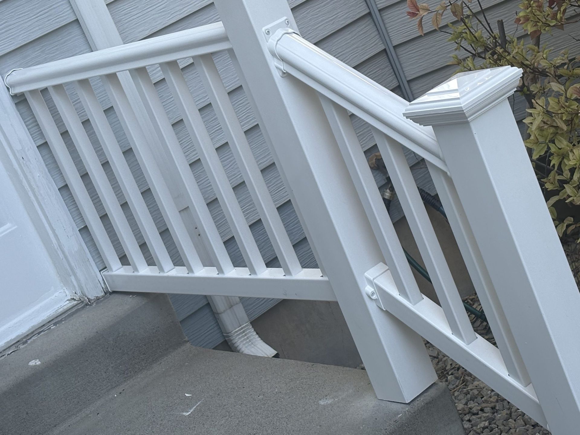 White wooden porch railing and steps beside a gray concrete walkway.