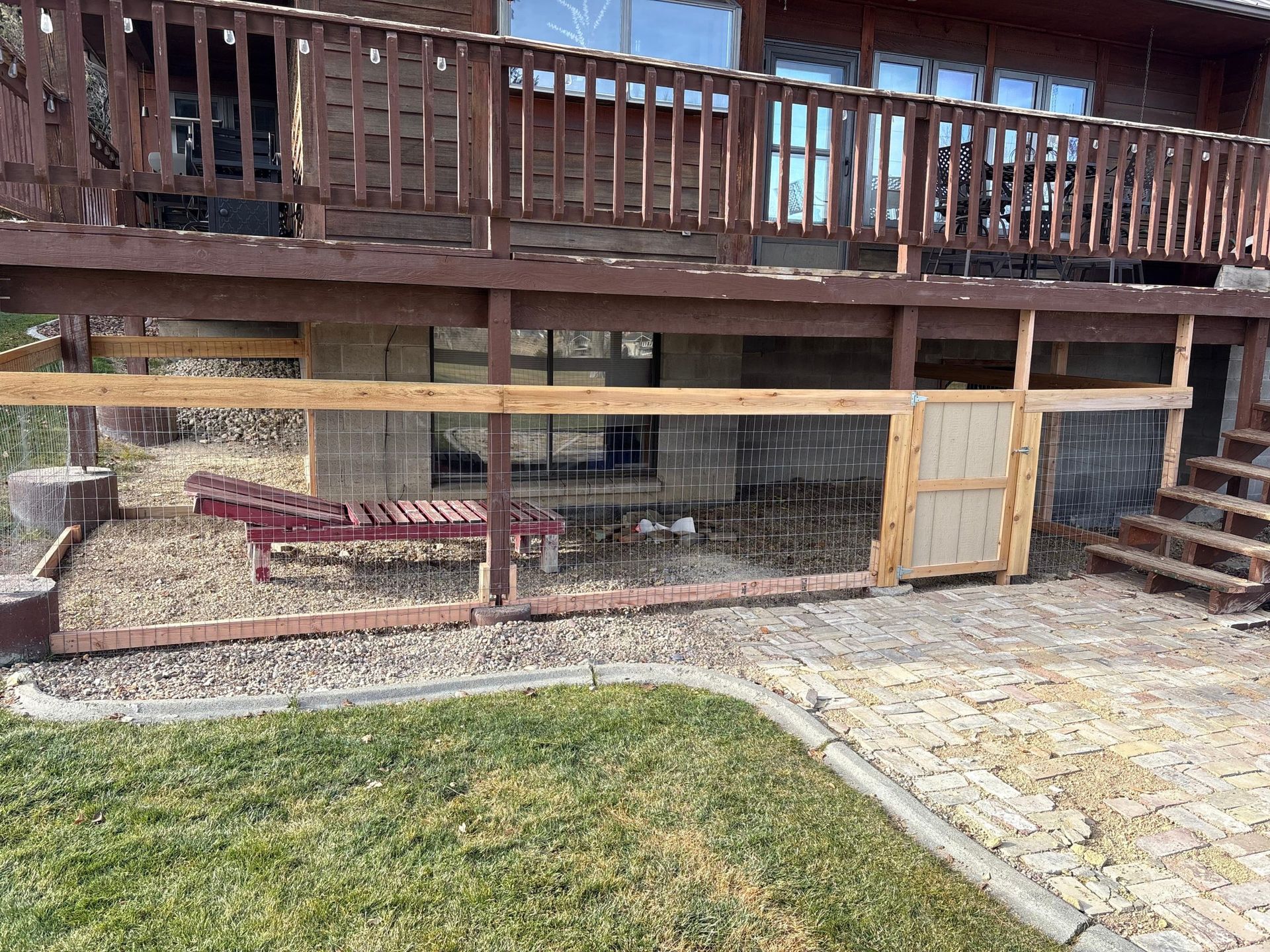 Wooden deck over a patio with a grassy yard, brick walkway, and stairs on the right
