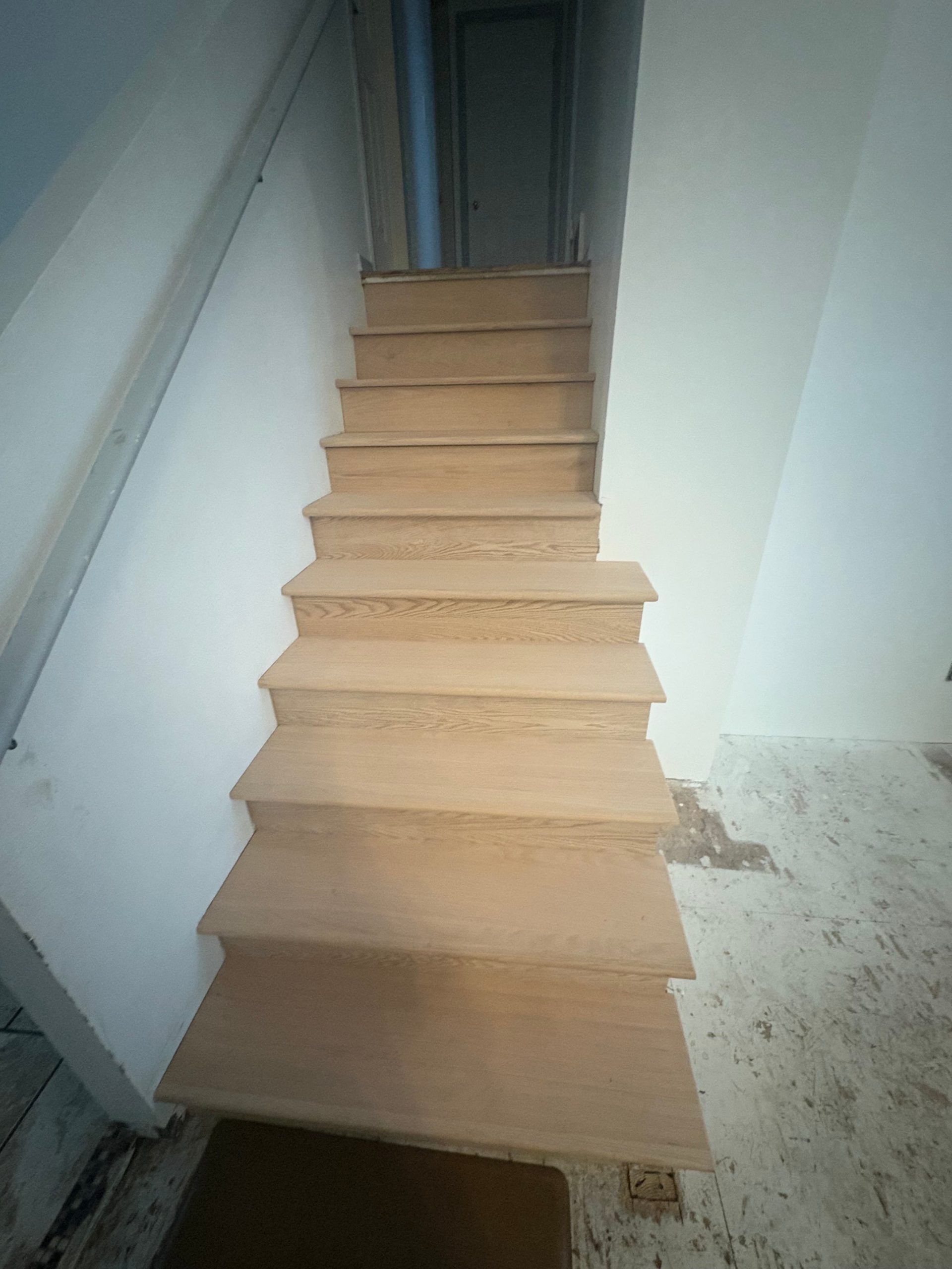 Narrow wooden staircase in an unfinished interior, leading up to a doorway.