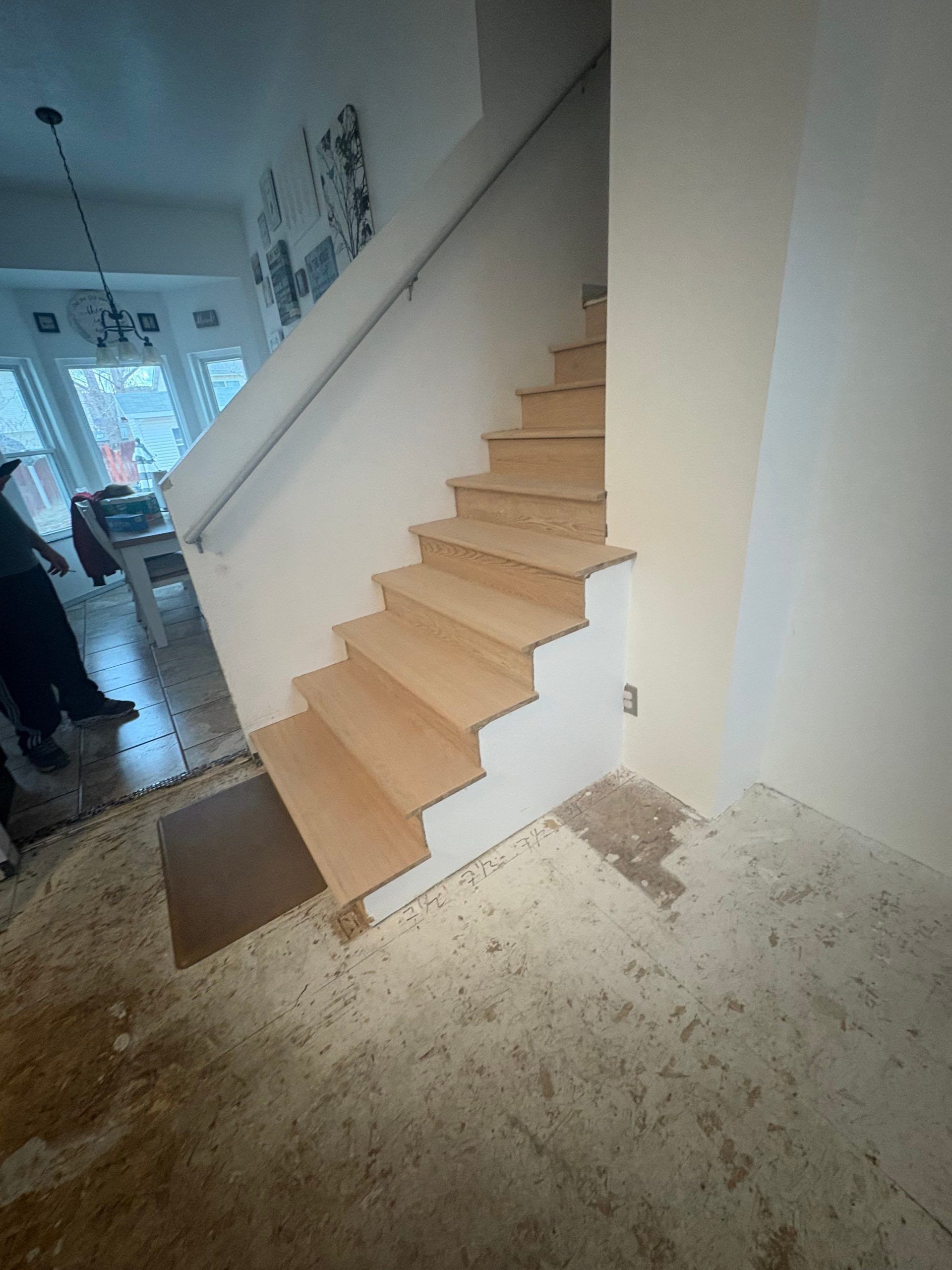 Indoor staircase with light wood steps and white walls in a sparsely furnished hallway.