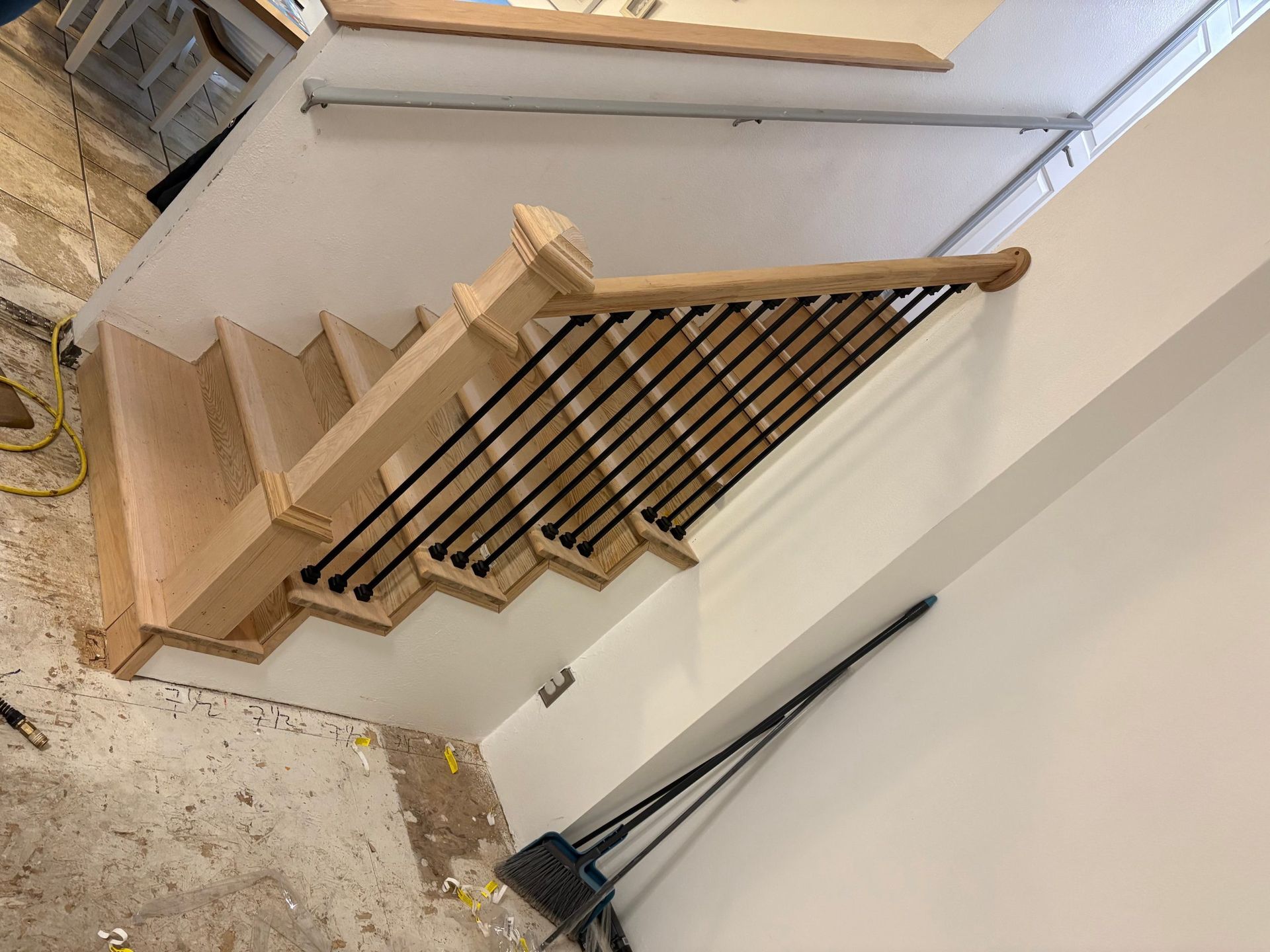 Wooden staircase under construction with black railings in a white interior hallway.