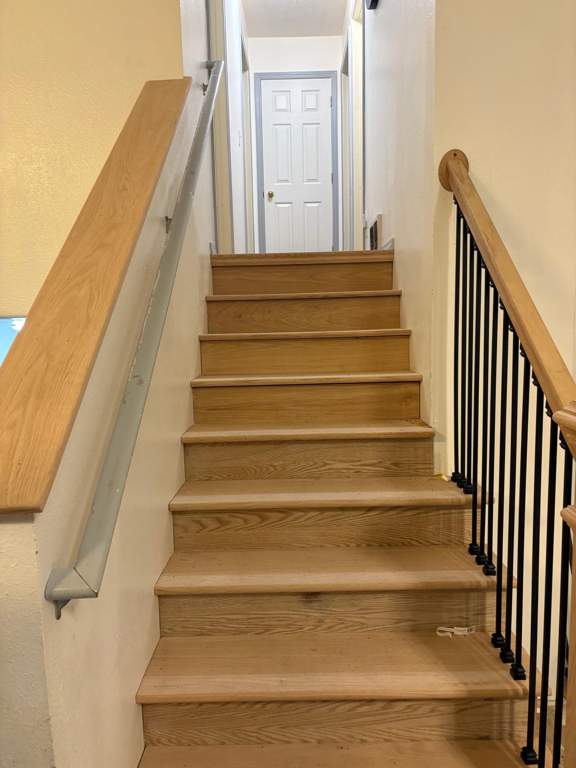 Carpeted indoor staircase with beige walls and black railing, leading to a white door at the top.