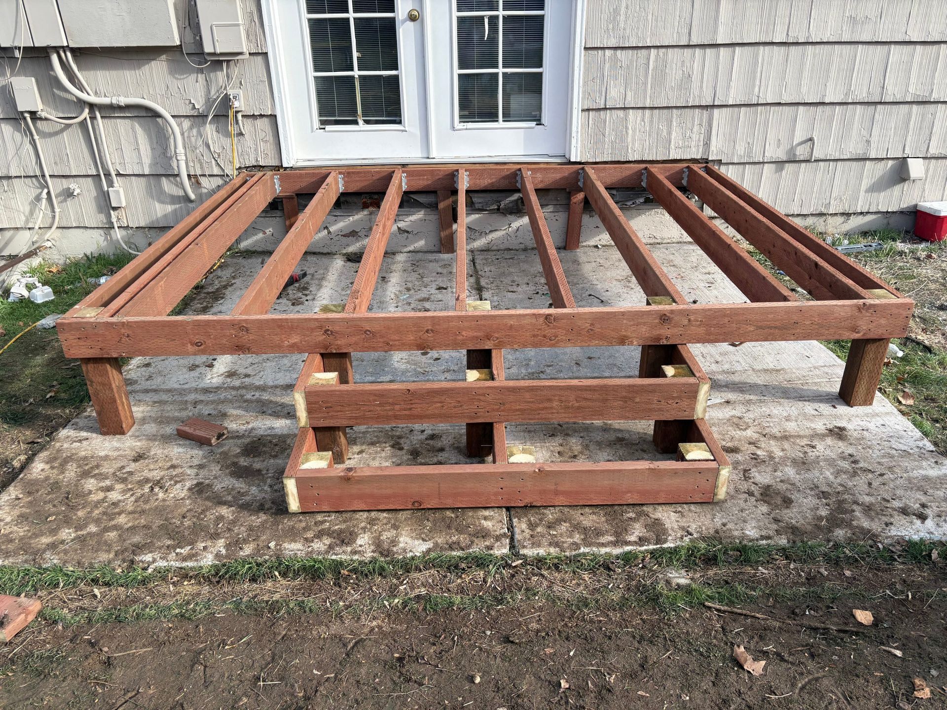 Wooden raised platform frame on cinder blocks beside a house wall and window.
