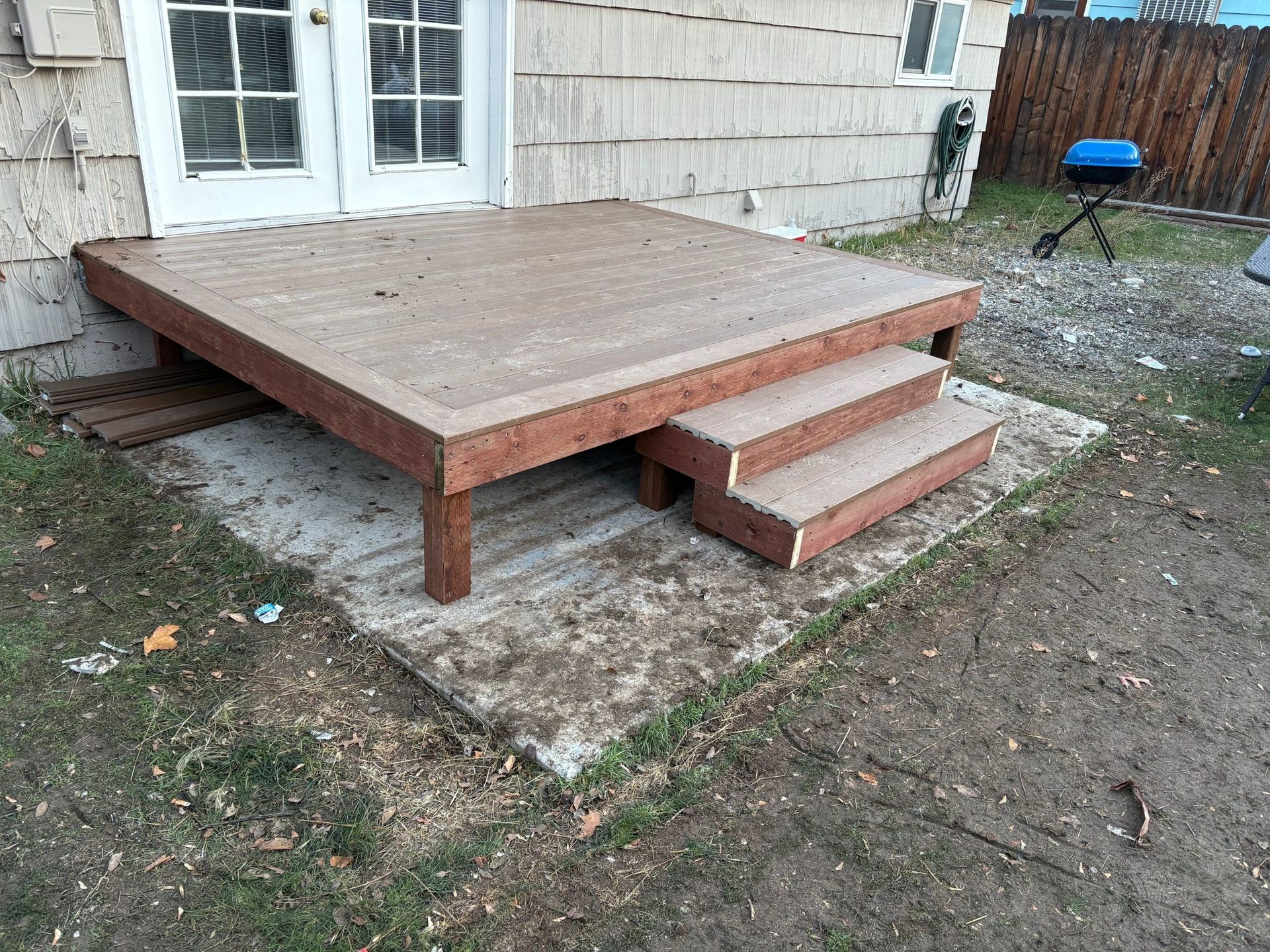 Wooden backyard platform deck with three steps beside a house exterior