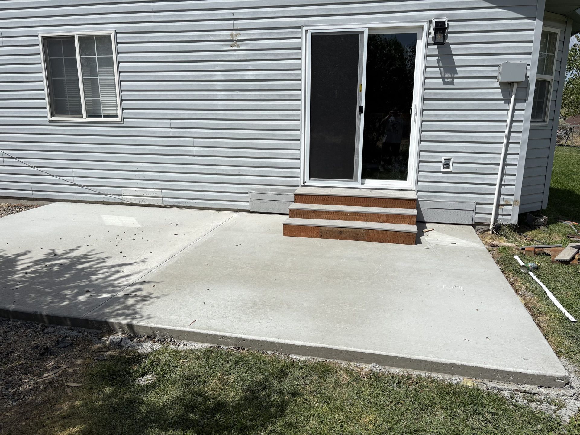 Concrete patio leading to a back door with small brick steps on a gray-sided house