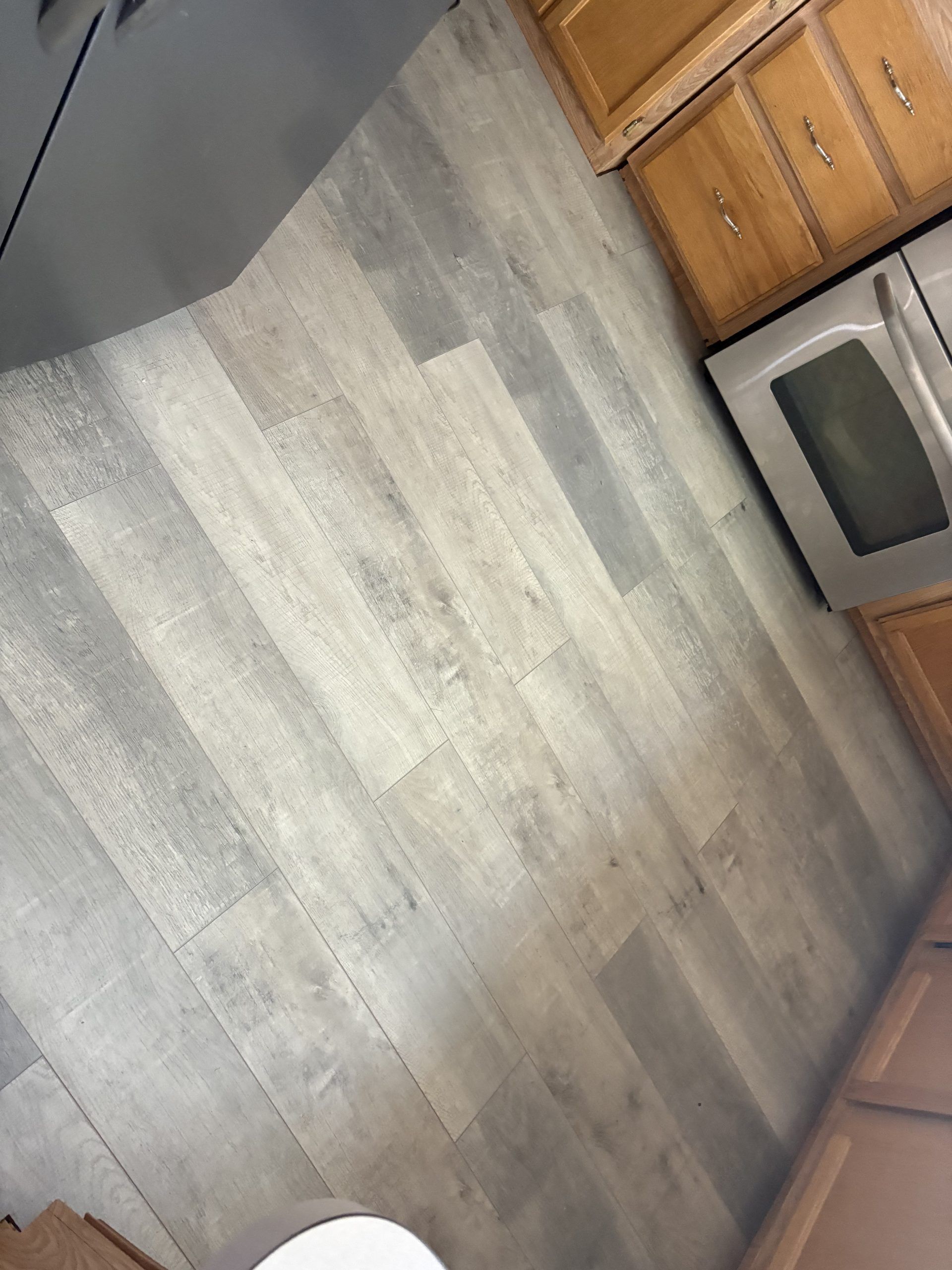 Kitchen with gray wood-look floor, wood cabinets, and a stainless steel oven.