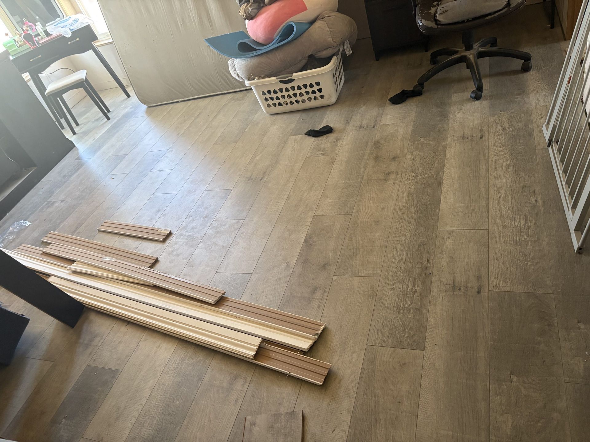 Wooden planks laid on a living room floor beside a chair and basket, with a pet gate nearby.