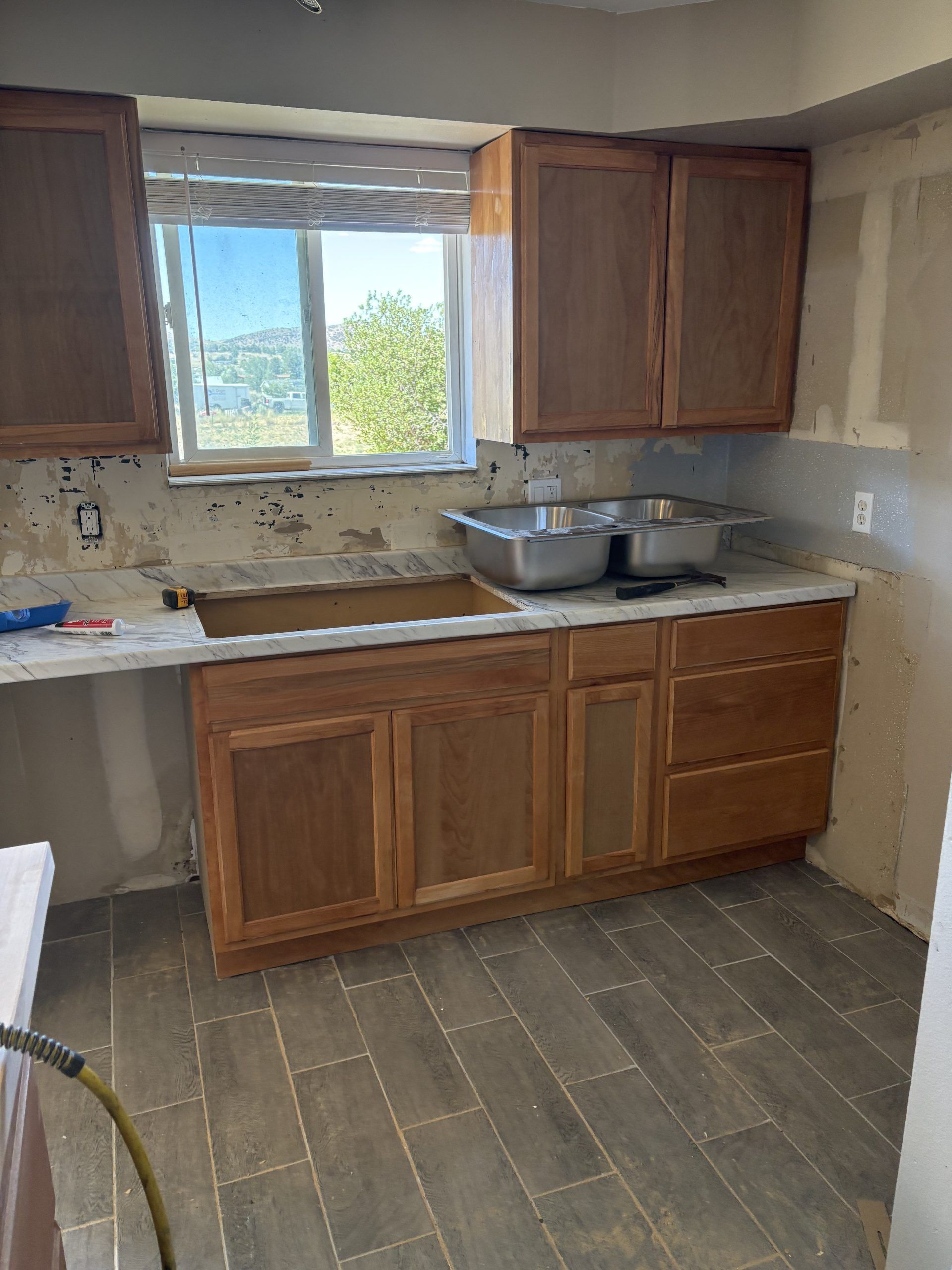Empty kitchen with wood cabinets, granite counters, sink, and a window overlooking trees and water.