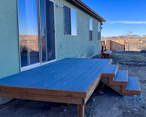 Blue-painted wooden deck beside a stucco house with sliding glass door and steps leading to the yard