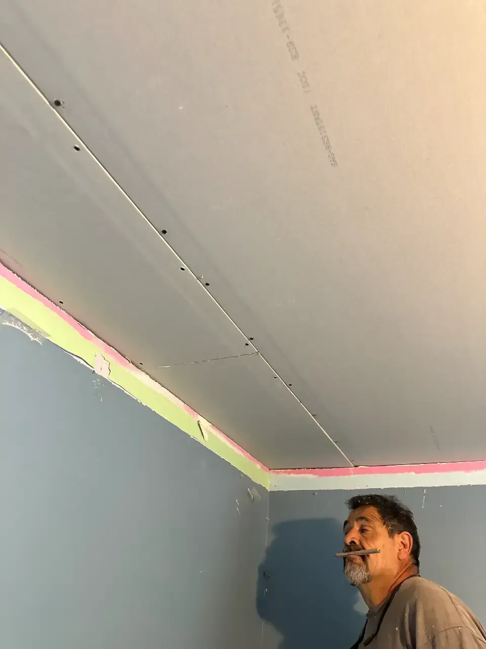 Man looking up at a ceiling corner with a visible crack or seam and a colored strip along the wall edge
