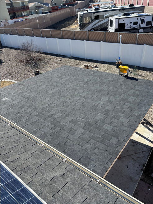 Rooftop with fresh gray shingles, solar panels at lower left, and a fenced yard in the background