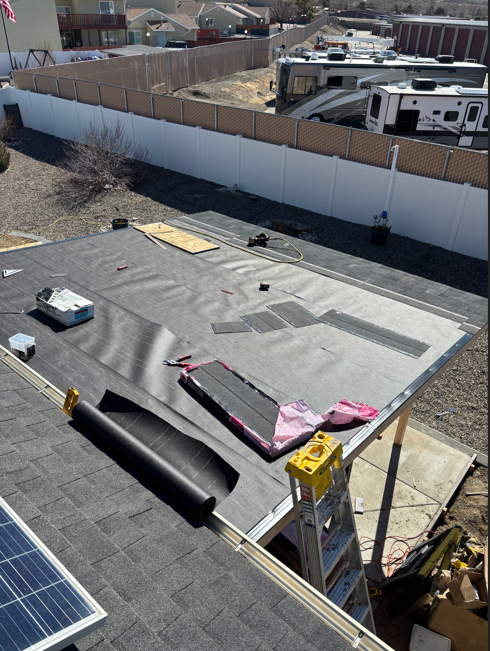 Rooftop under construction with gray roofing, pink membrane, ladder, and solar panel in foreground