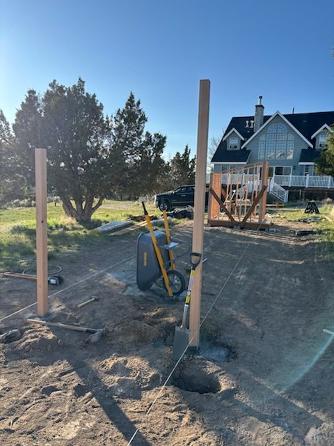 Outdoor construction site with posts, wheelbarrow, and house in the background.