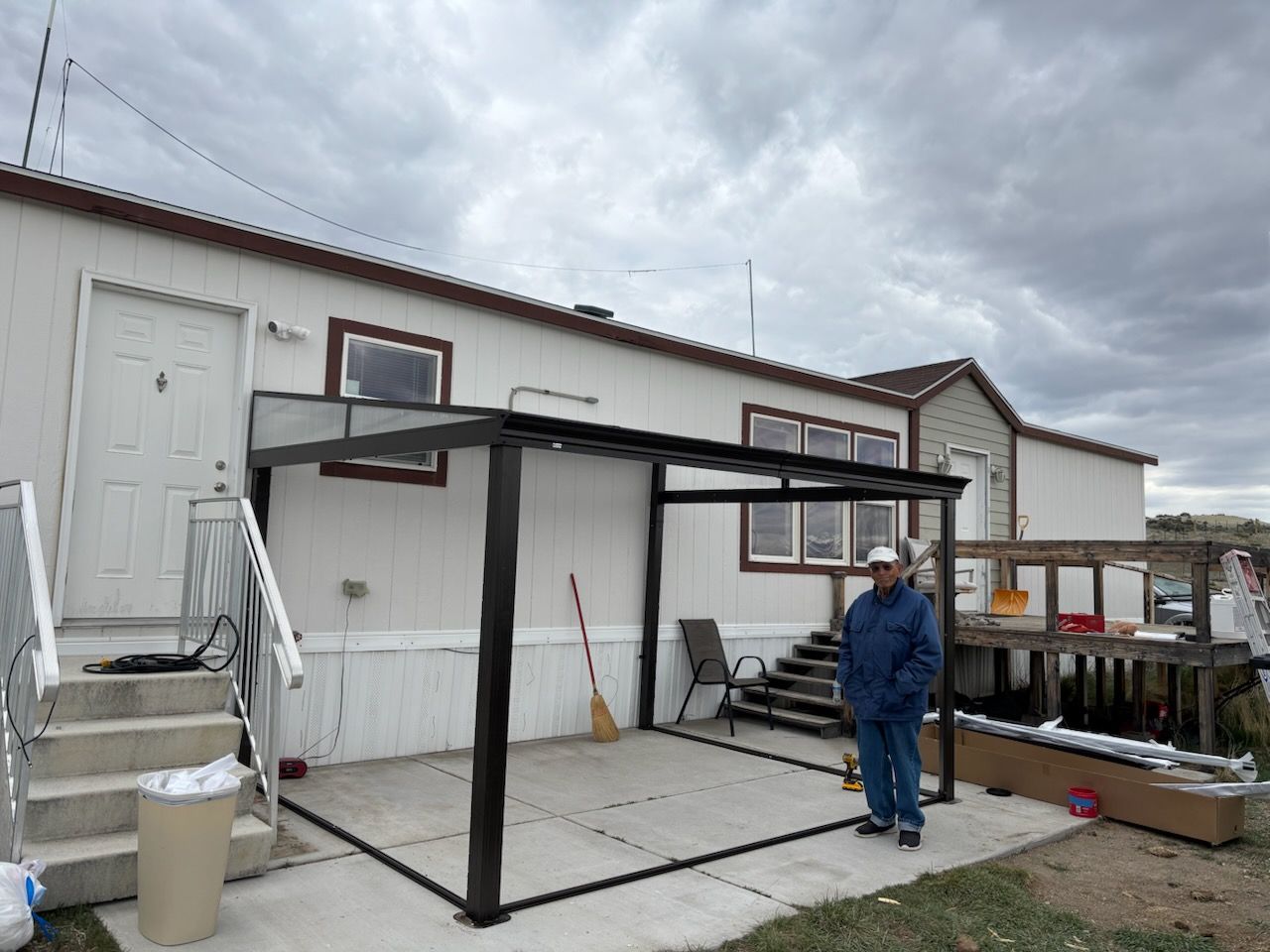 Person in blue jacket standing beside a black metal frame on a rooftop patio under cloudy skies.
