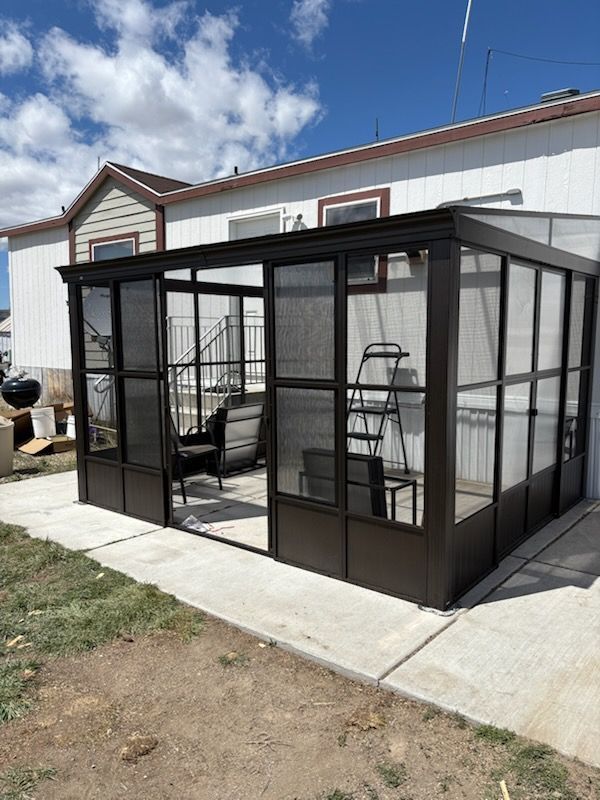 Black screened porch enclosure attached to a house beside a concrete patio.