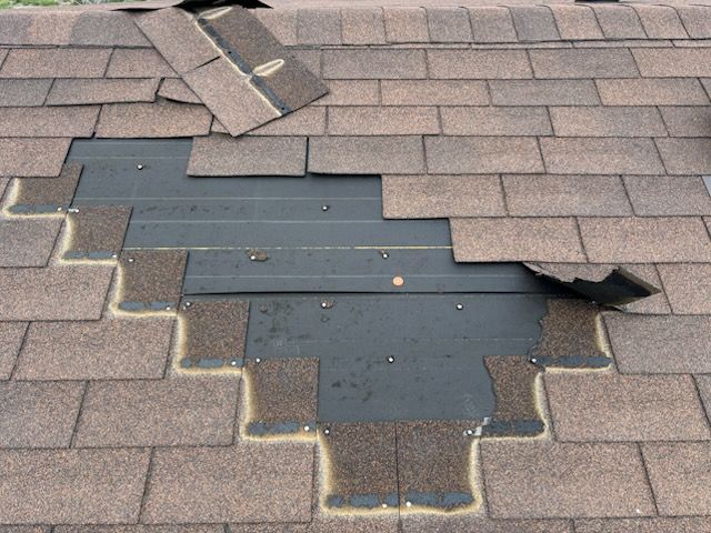 Damaged shingle roof with a large patched area of dark roofing material and loose shingles