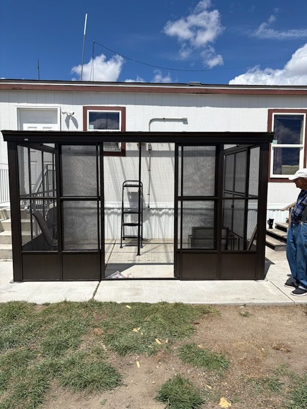 Black metal enclosed patio structure with mesh doors on a concrete slab beside a house