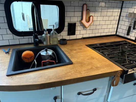 Kitchen sink and stovetop with wood countertop, white tile backsplash, and a pumpkin in the sink.