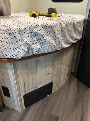 Small round wood-paneled bed or seating nook with a white dotted blanket and yellow dumbbells on top.