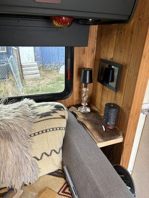 Cozy camper van interior with wood paneling, sofa, lamp, shelf, and window view
