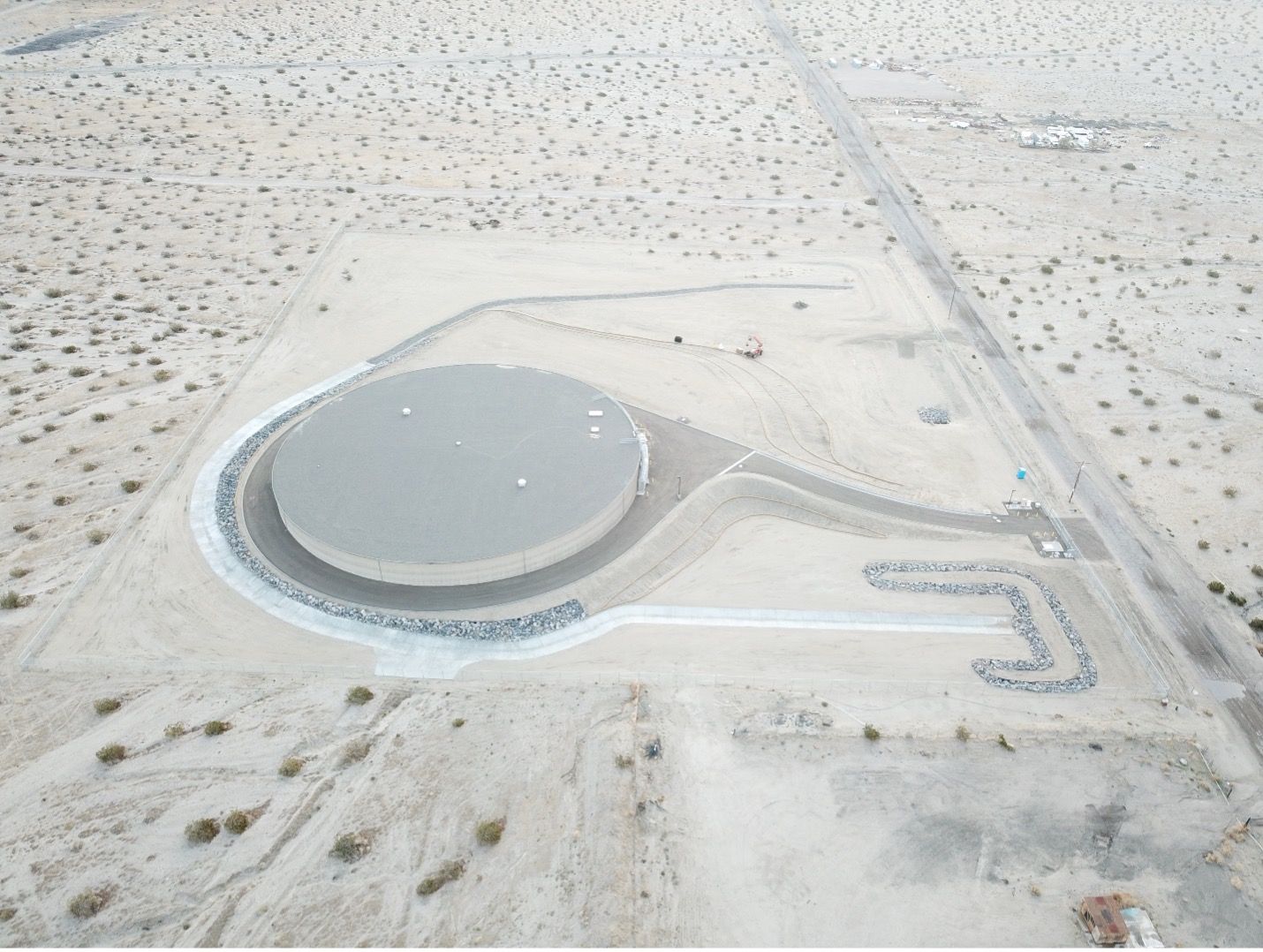 Aerial view of a large circular industrial tank in a sandy desert site with access roads.