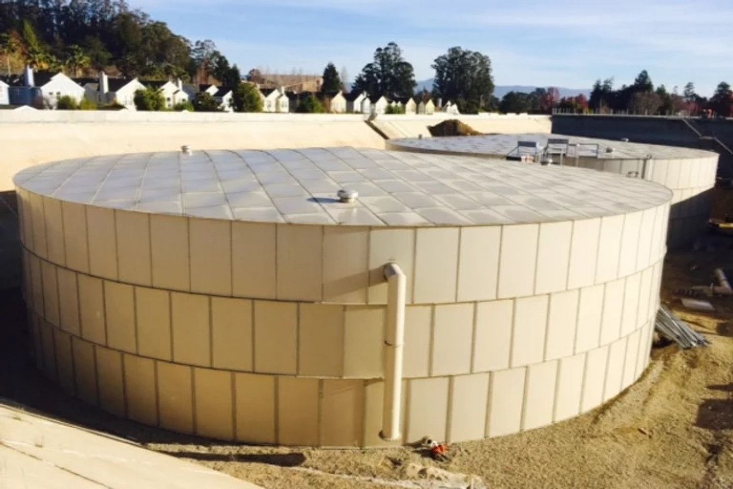 Large circular beige industrial storage tank under construction on a dirt site