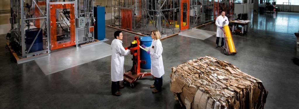 Workers sorting stacked cardboard in a warehouse with metal racks and orange machinery