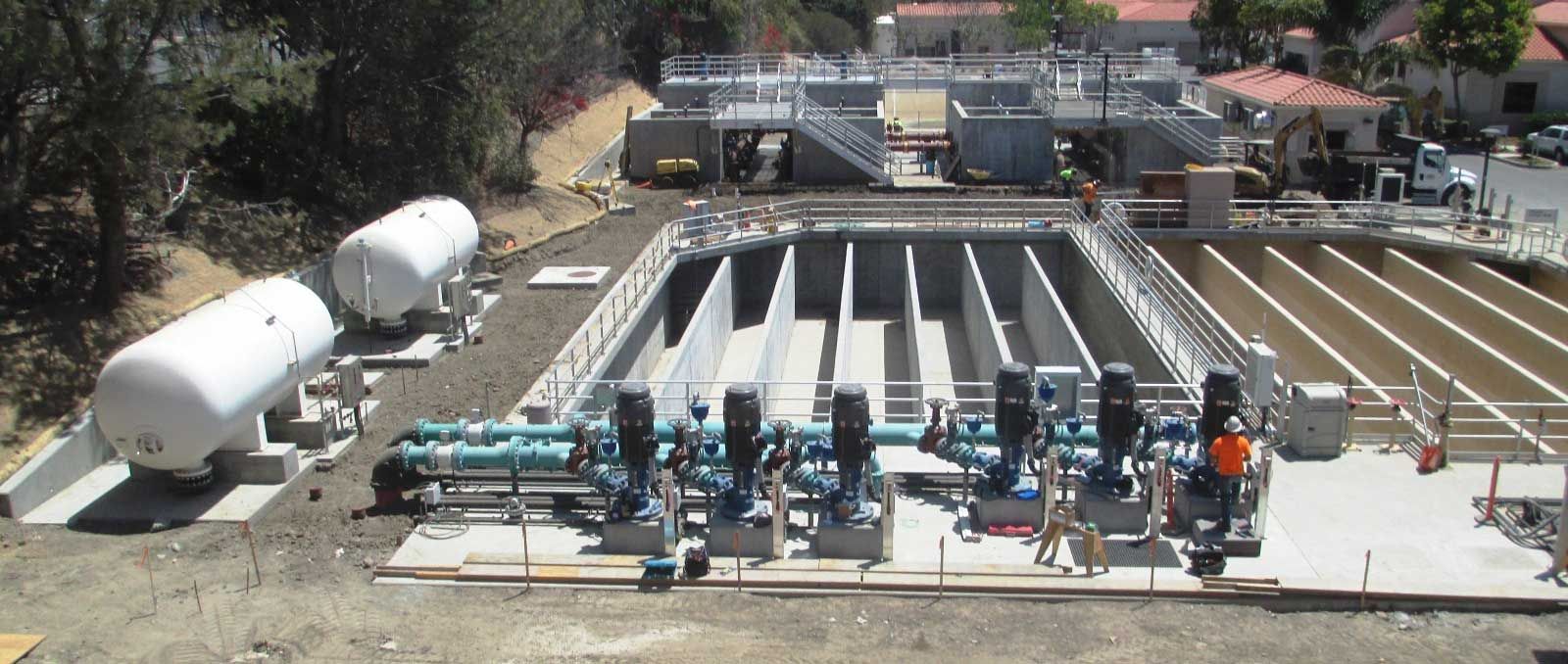 Construction site with rows of concrete culverts, tanks, and heavy equipment in an industrial yard