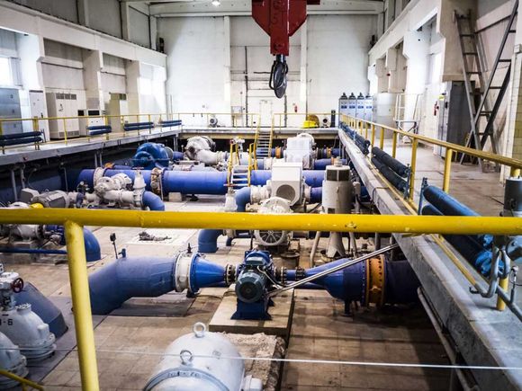 Industrial pump room with large blue pipes, valves, and overhead crane in a bright utility facility