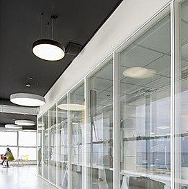 Modern office corridor with glass walls, white desks, and round ceiling lights