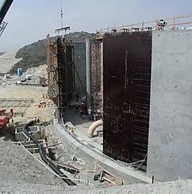 Industrial construction site with tall concrete retaining walls and scaffolding on a hillside.