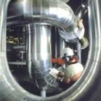 Worker inspecting large shiny industrial pipes in a machinery room