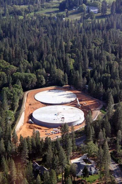 Two large white storage tanks under construction in a forested clearing, surrounded by trees.