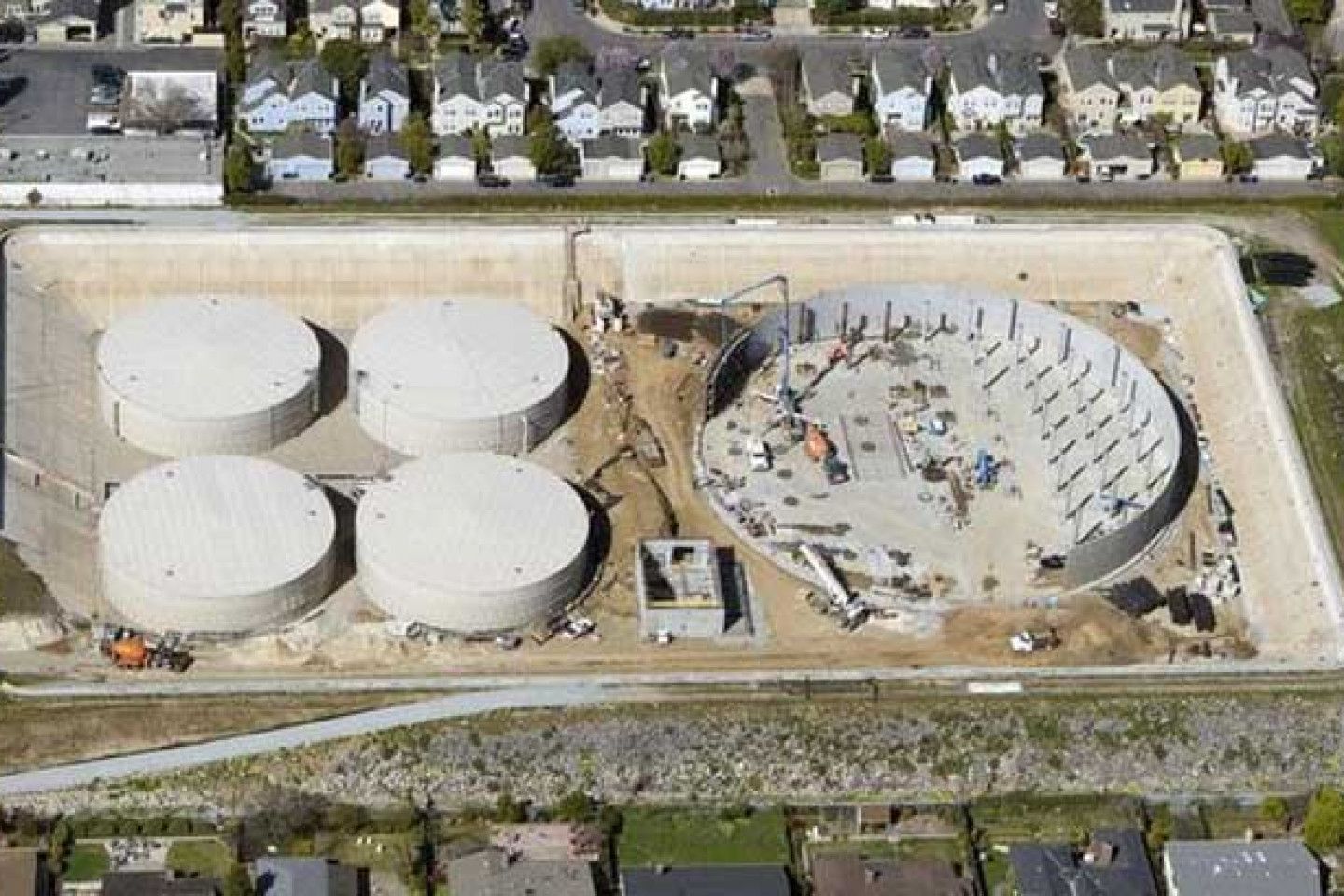 Aerial view of a wastewater treatment plant with four white tanks and a large circular basin under construction