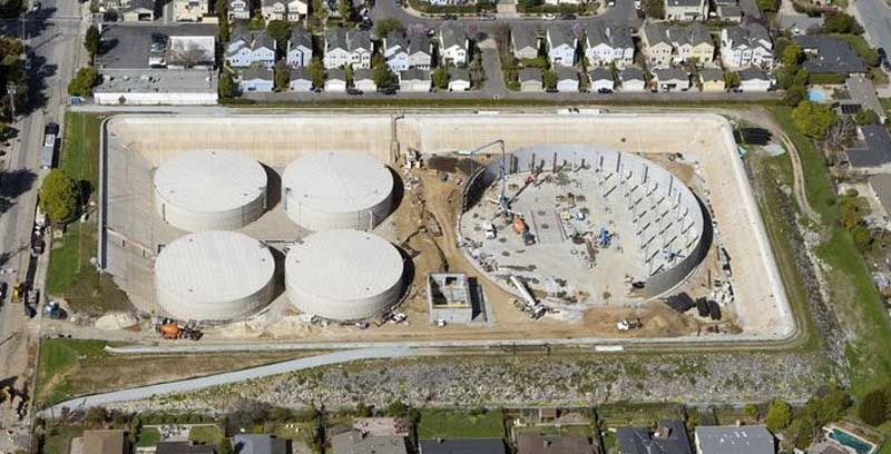 Aerial view of an industrial site with four white storage tanks and a large circular concrete structure.