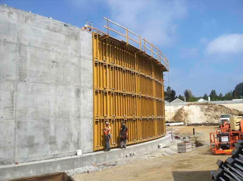 Construction workers beside a large concrete wall and yellow formwork at a building site