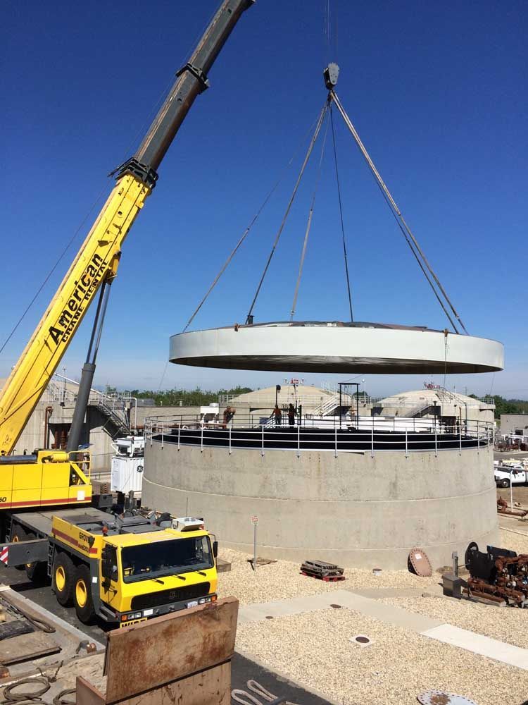 Crane lifting a large concrete ring onto a circular structure at a construction site