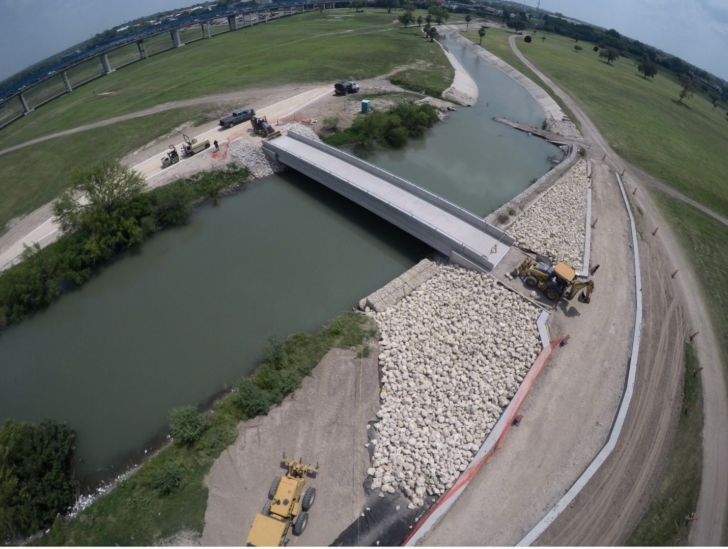 Aerial view of a bridge over a canal with construction equipment and riprap embankments.