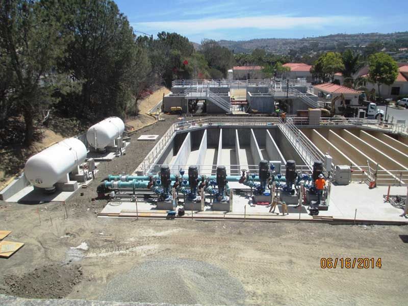 Industrial water treatment facility with tanks, pipes, and equipment outdoors in a dry landscape.