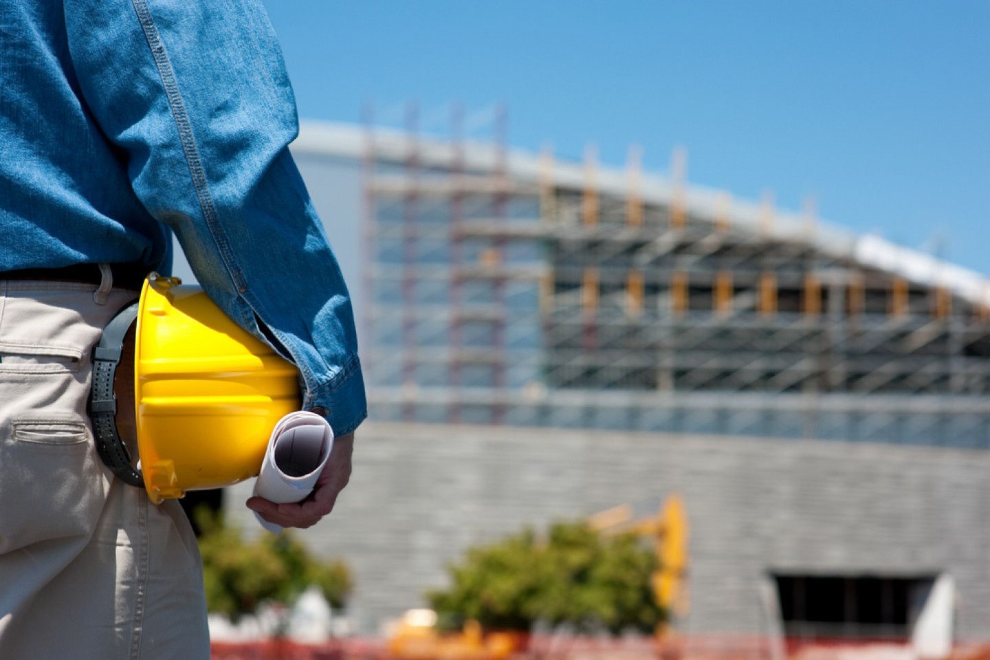 Construction worker holding yellow hard hat at building site under construction