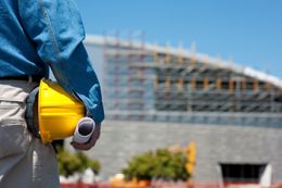 Construction worker holding yellow hard hat at building site under construction