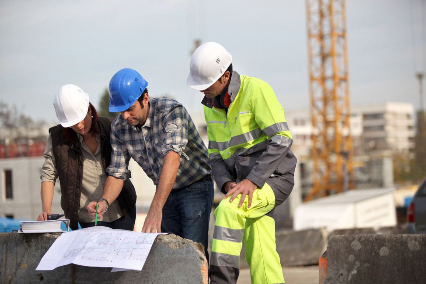 Three construction workers in hard hats reviewing plans on a building site.