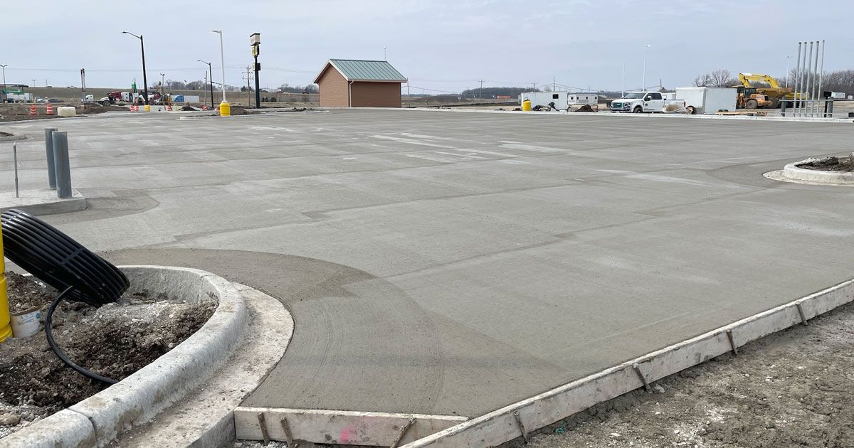 Newly poured concrete parking lot with a small brown building in the background.