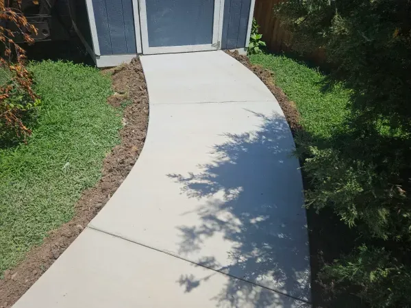 Curving concrete sidewalk leading to a building entrance, bordered by grass and landscaping.