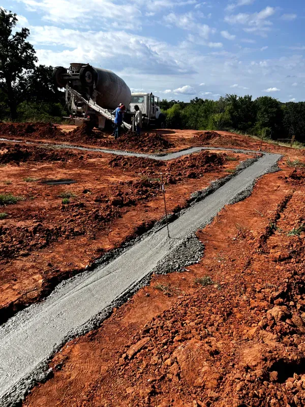 Concrete being poured into a trench at a construction site. A cement truck is visible.