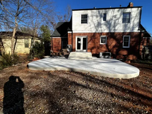 Back of a two-story brick and white house with a newly poured concrete patio. A person is taking the photo.